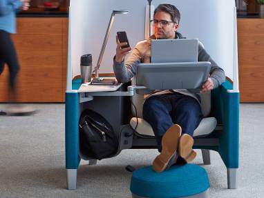 A man in a Brody WorkLounge working on a laptop and checking his phone