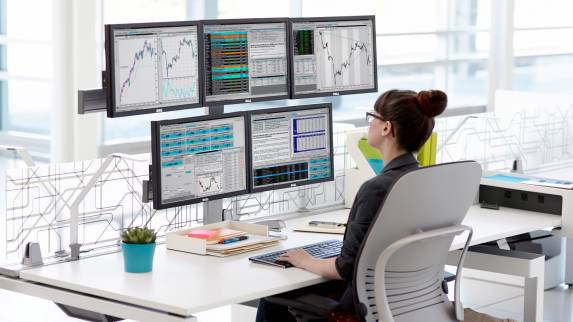 Woman sitting at a desk in front of five displays supported by Plurio's 26″ column