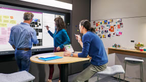 Three persons collaborating while drawing on interactive ideation hub surface
