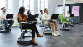 6 people inside a classroom seated on Node chairs with their laptops