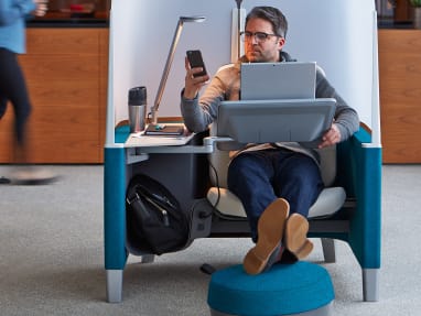 A man in a Brody WorkLounge working on a laptop and checking his phone