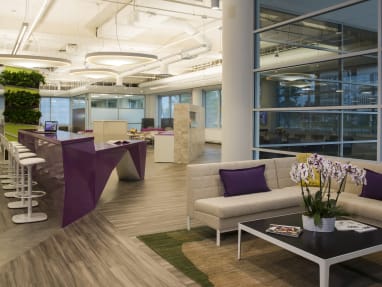 Open space with beautiful furniture such as beige large sofa with purple pillows, purple tall table with white stools.