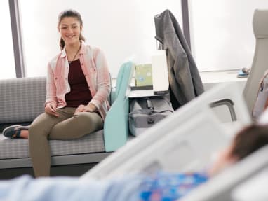 Young lady sitting on a Surround sleeper sofa in a patient room