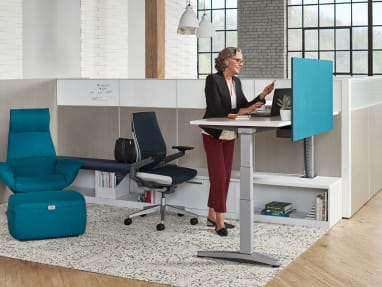 Woman working on a Ology height-adjustable desk with blue Universal Modesty Screen