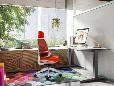red Steelcase Series 1 with head rest inside a private room with white desk, Dash light on the desk and colorful rug.