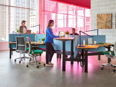 Three people work at a group of workstations created with Ology height adjustable desks, Gesture desk chairs, and Dash task lights