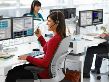 A group of people sitting on gray Leap chairs in front of their desks with headsets on, looking at Eyesite dual monitor.