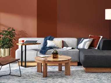 A collection of West Elm Work products in a lounge setting, including a Conover Plinth armless sofa, Conover Plinth ottoman, Boerum coffee table, Slope lounge chair, and Linear C-Table
