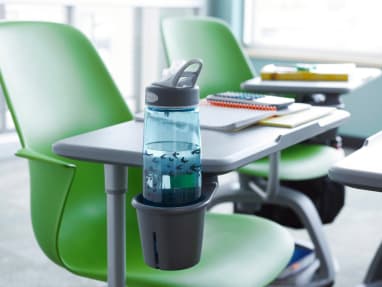 A water bottle is placed in the cupholder attached to the worksurface of a green Node tripod-base chair