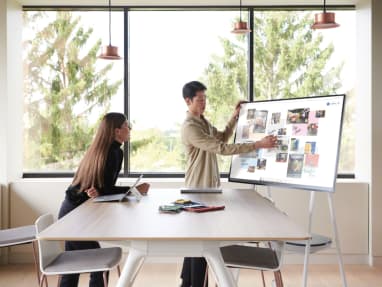 A man presents information at a Steelcase Roam while a woman listens while standing next to a Potrero415 table with Montara650 stools