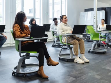 6 people inside a classroom seated on Node chairs with their laptops