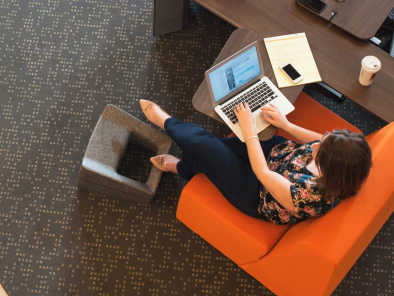 Overhead view of a woman working with a laptop on a Campfire Skate Table while sitting on a Campfire Half Lounge