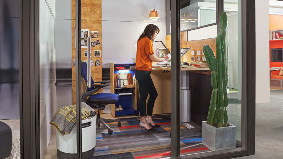 Woman on a creative private work area with adjustable height desk and glass walls