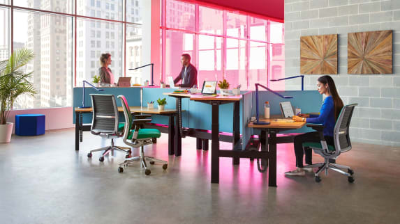 Three people work at a group of workstations created using Steelcase Ology benching and Gesture desk chairs