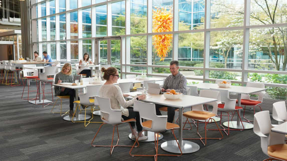 Shortcut X-base chairs with orange and yellow legs are placed around Steelcase Groupwork tables in an office cafe