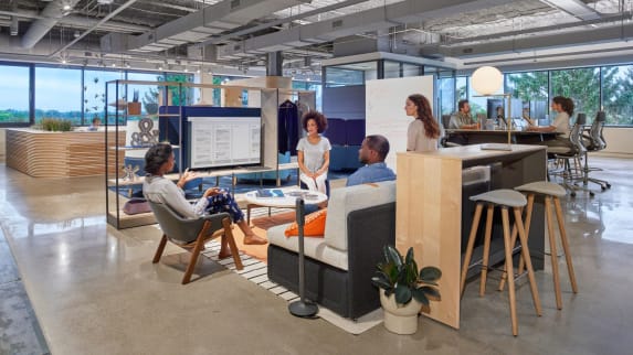 Open-space to informally discuss ideas, equipped a gray lounge sofa, a gray chair and gray Enea Cafe Stools in front of a TV screen.