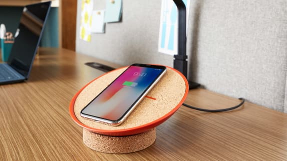 A phone charges on a SOTO wireless charger placed on a desk