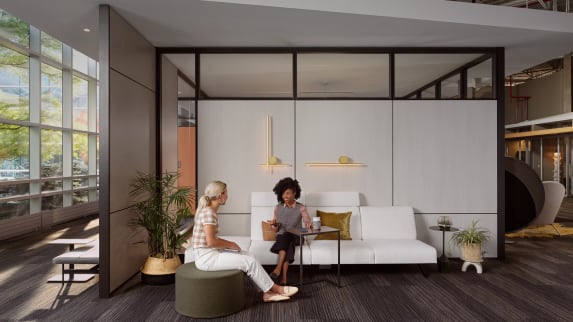 two women talking while seated on a white sofa with Everwall behind