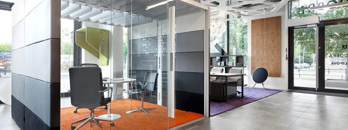 An Orangebox Air pod is seen in an office setting next to a lounge with three desk chairs arranged around a table