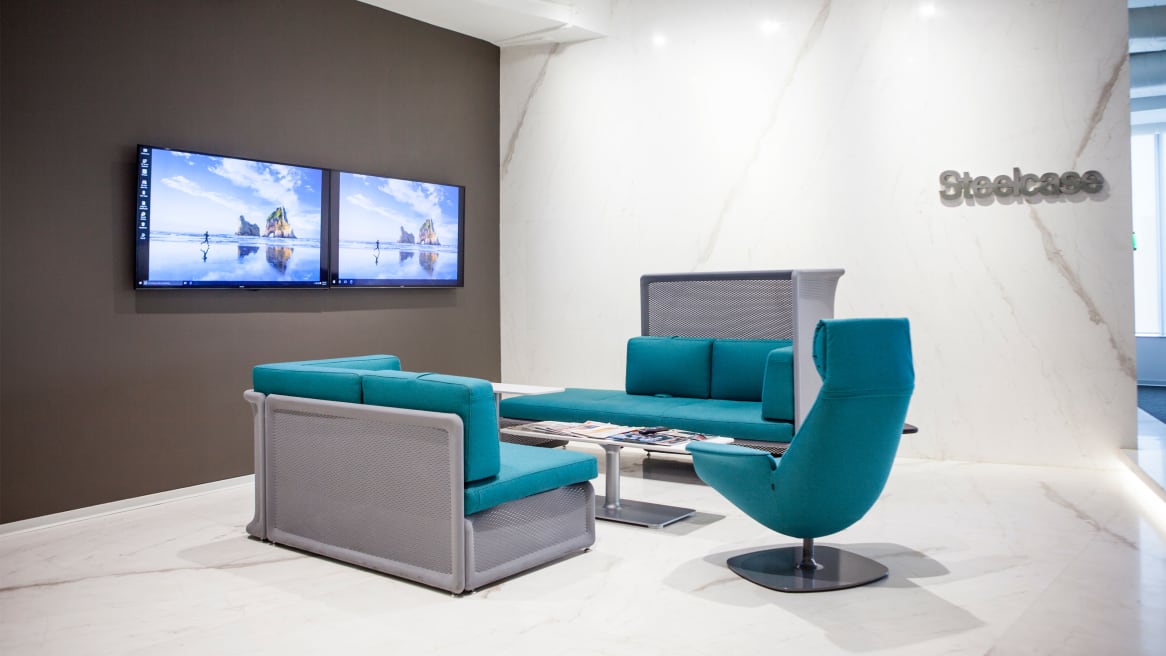 Setting with two blue Lagunitas sofas and a blue Massaud chair in front of two Surface Hub screens