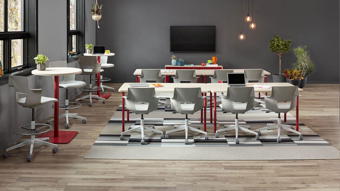 Four rectangular Simple Tables with red legs paired to form two long tables with white Shortcut office chairs and two round standing height Simple tables with red bases and accompanying Shortcut stools