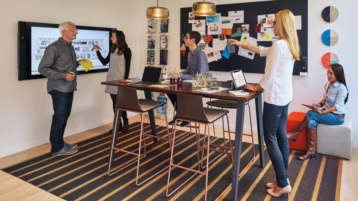 team collaborates in a small conference room with interactive screen
