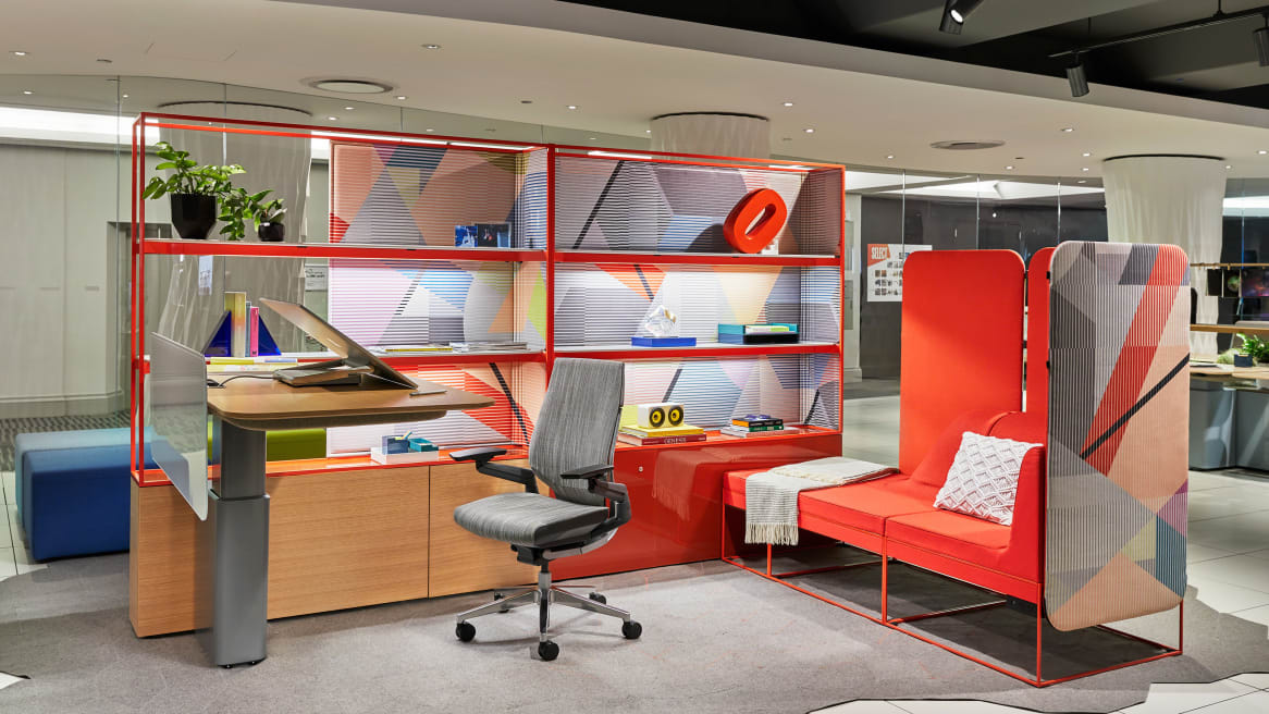 At NeoCon 2018, a display features a workstation created using Steelcase Mackinac, a Gesture desk chair with gray upholstery, and Umami lounge seating with orange upholstery