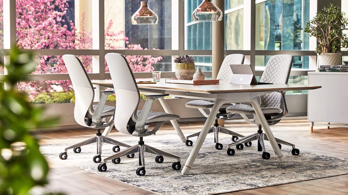 Four SILQ desk chairs with gray upholstery are arranged around a Potrero415 table in a collaborative space near a window