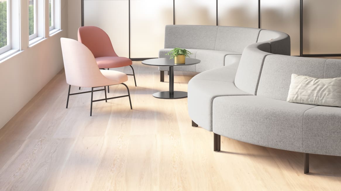A Circa lounge seating system from Coalesse with gray upholstery with two pink chairs and a round gray table nearby
