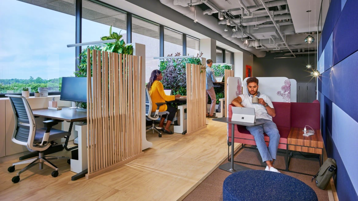 People work in an office featuring Umami lounge seating, Steelcase Think desk chairs, and height adjustable desks