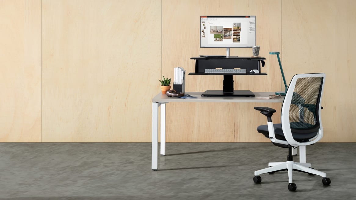 An Active Lift Riser from Steelcase is used on top of a Currency Martin desk with an Amia chair next to it
