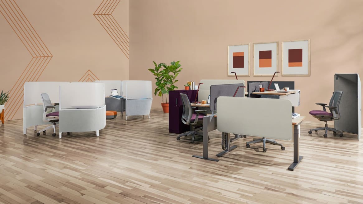 Brody WorkLounge and Desk placed next to a group of workstations created with Migration height-adjustable desks, Amia Air chairs, and Sarto screens. A gray Clipper Screen is also seen next to a chair.