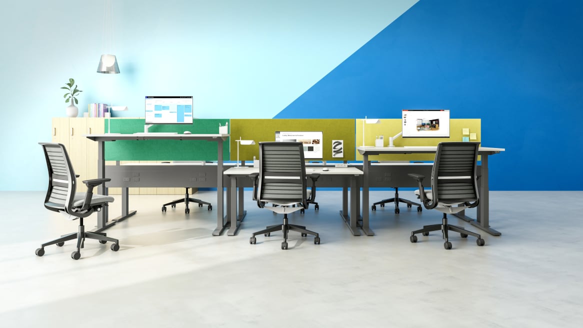 A group of workstations featuring Migration SE height-adjustable desks, Universal privacy screens, and Think desk chairs