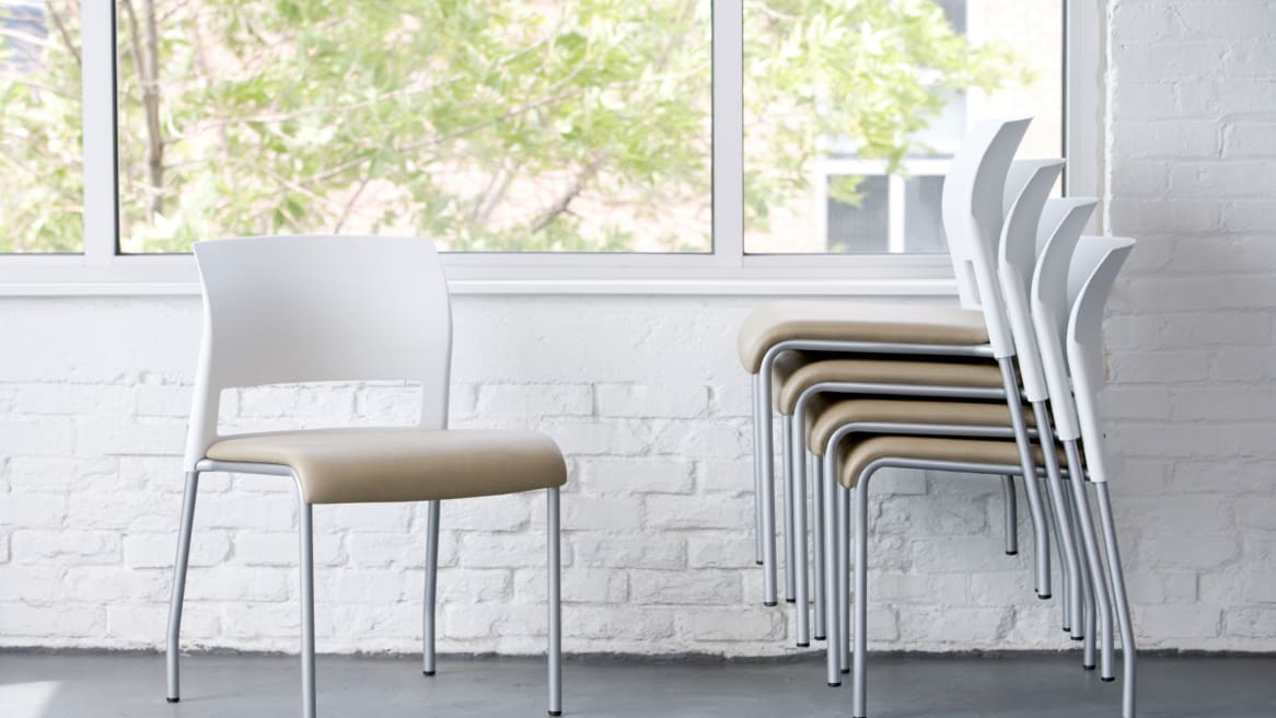 A single Steelcase Move chair next to a few Move chairs stacked together in front of a white brick wall