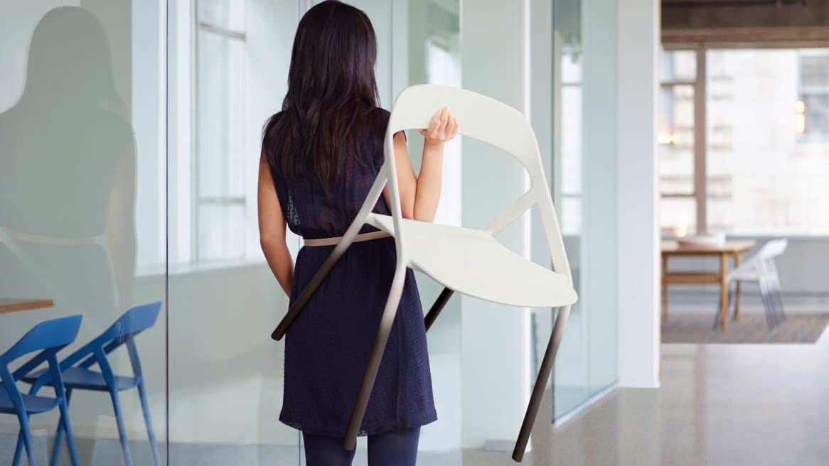 A lady carrying a white LessThanFive Stackable Guest Chair over her shoulder