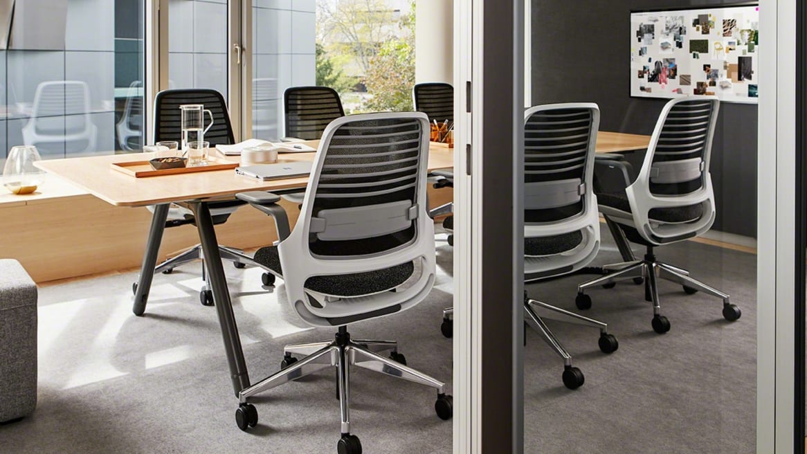 inside a meeting room there is a large wooden table and several black Series 1 chairs