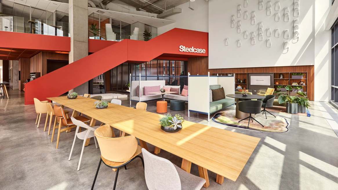 Open space with wooden table and orange staircase with steelcase logo.