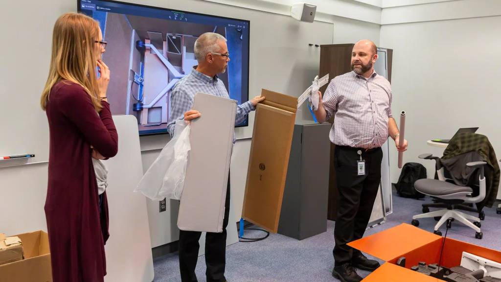 two men and a woman holding and unboxing new products such as screens