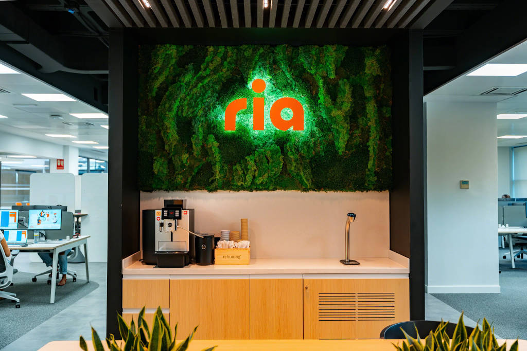 Ria logo illuminated on a mossy background in a work environment