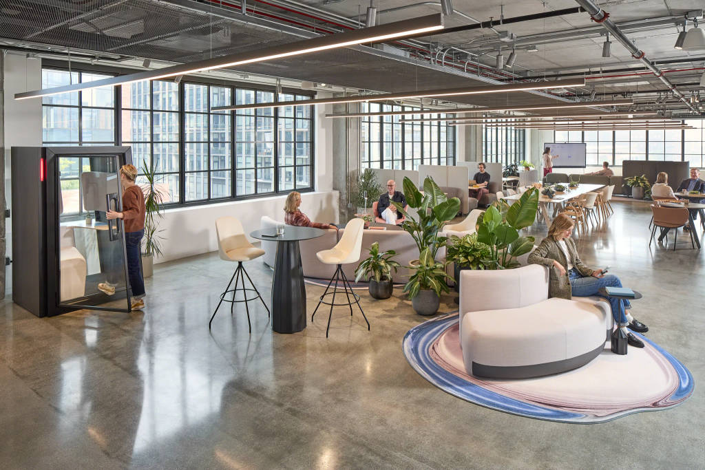 Open office with lounge seating, collaboration areas, phone booth, and plants supporting flexible work.