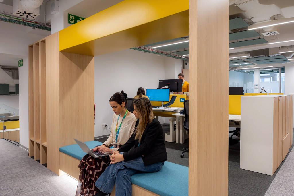 Informal seating area in a modern office, with people using a laptop near workstations