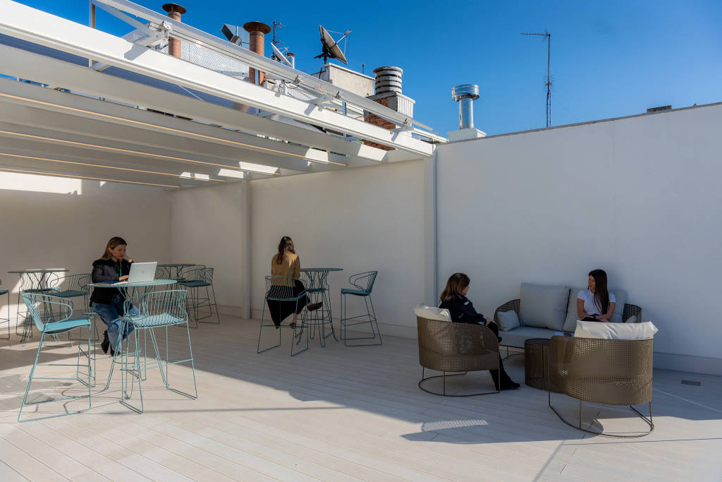 Rooftop terrace with tables and lounge seating, where people are working and talking