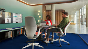 Two people sit in SILQ chairs by Steelcase in a private meeting room while looking at monitors