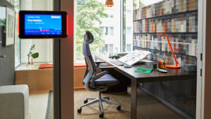 A private enclave by a window at LINC offices in Munich includes a Gesture desk chair with headrest and an orange Dash Mini desk lamp from Steelcase