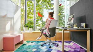 A woman in an office area with a colorful rug sits in a SILQ chair by Steelcase with her back turned toward the camera