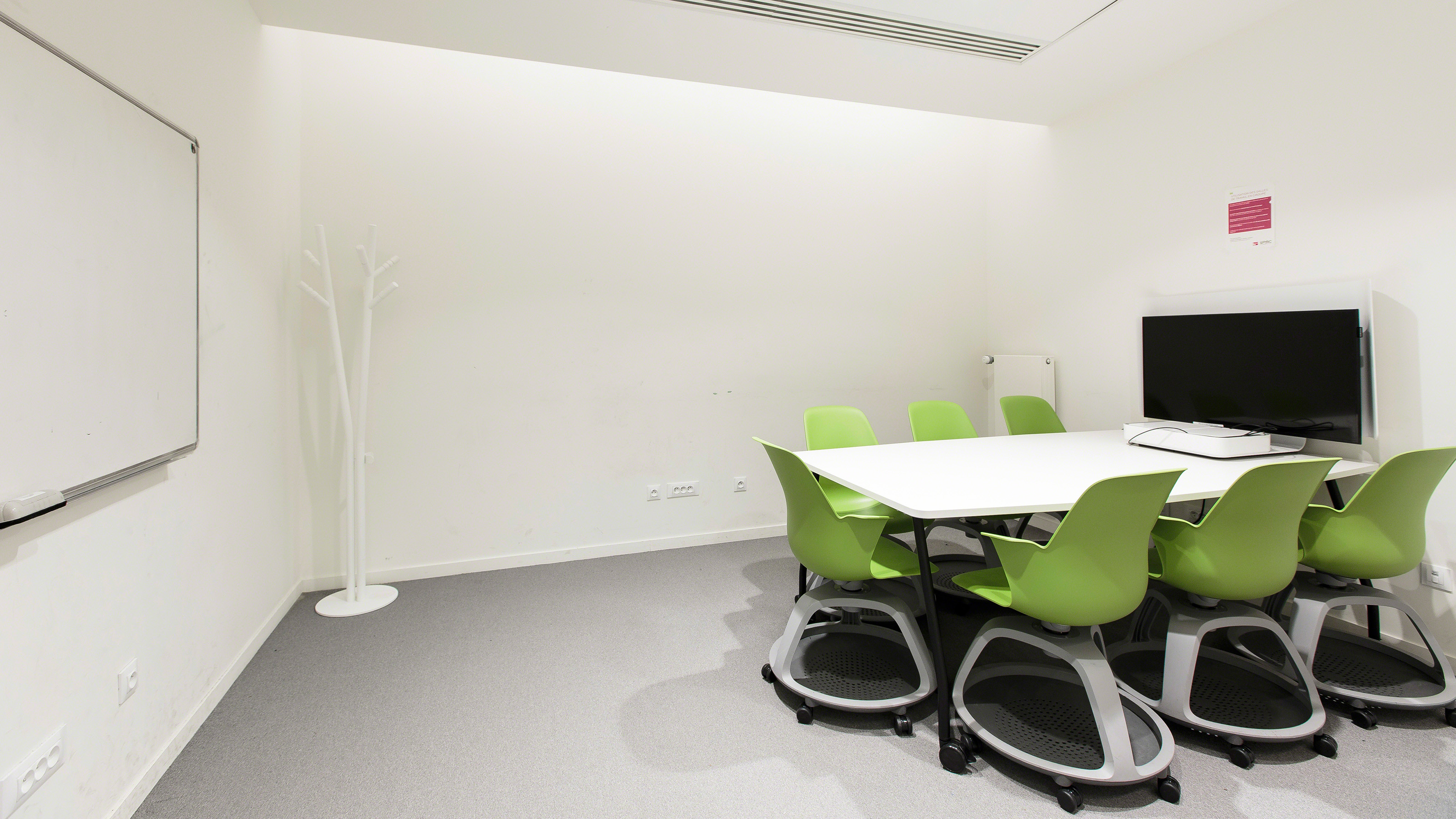 small conference room with green chairs arranged at a table with a screen at one end and a whiteboard on the opposite wall
