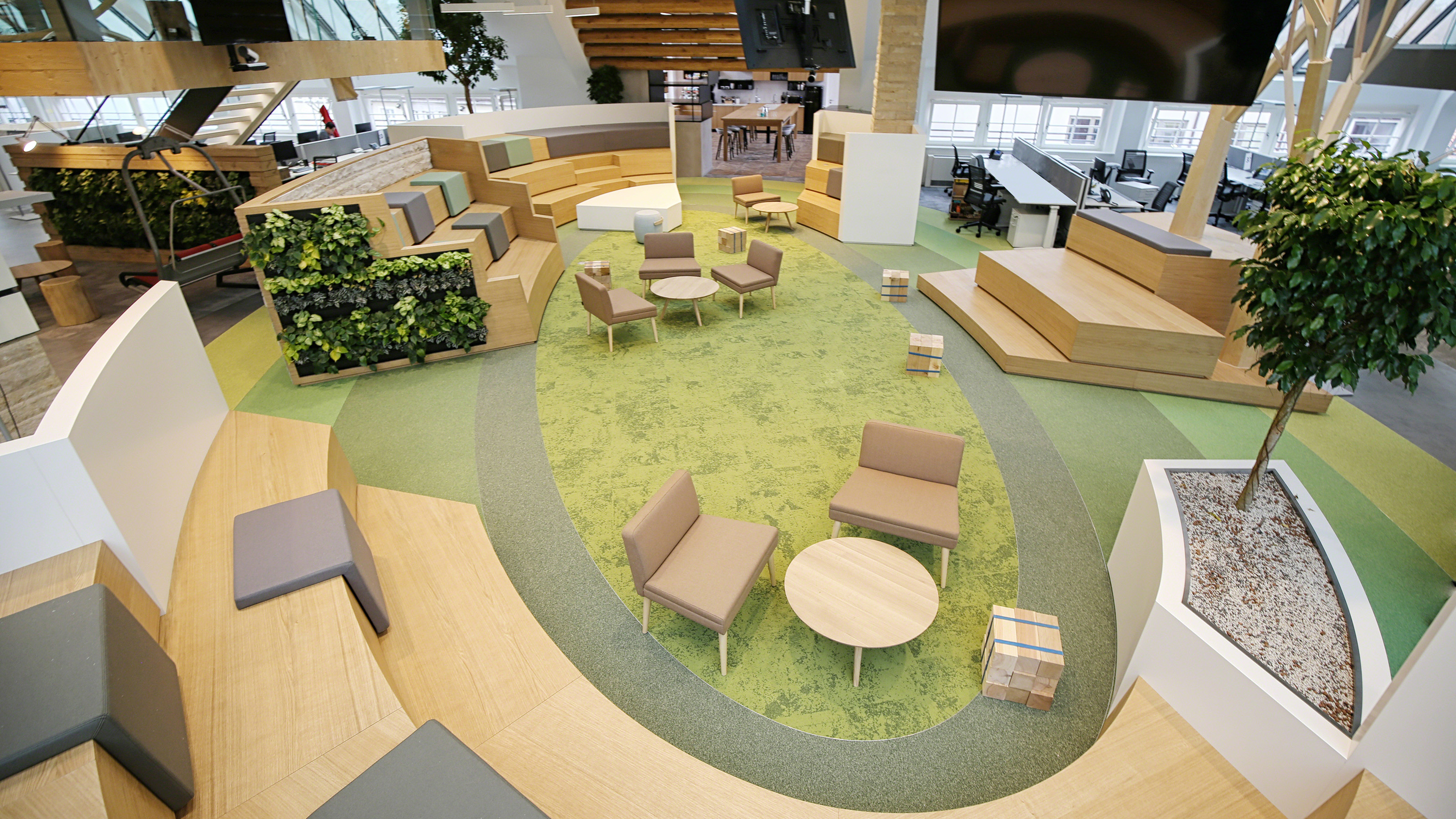 Open common space with green rug, rows made of wood for people to sit and coffee tables