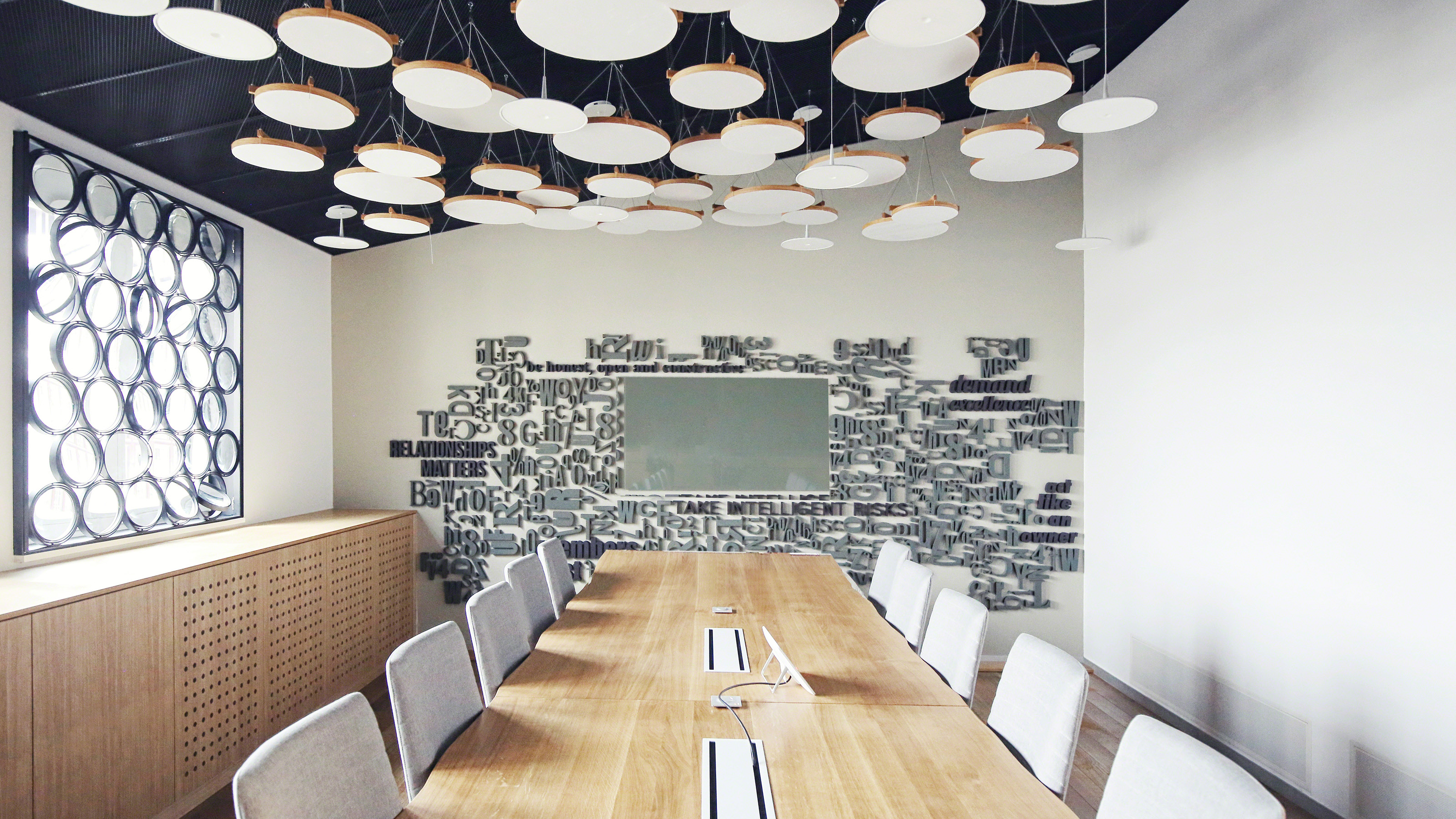 Meetings room with a large wooden table, gray chairs and words on the wall.