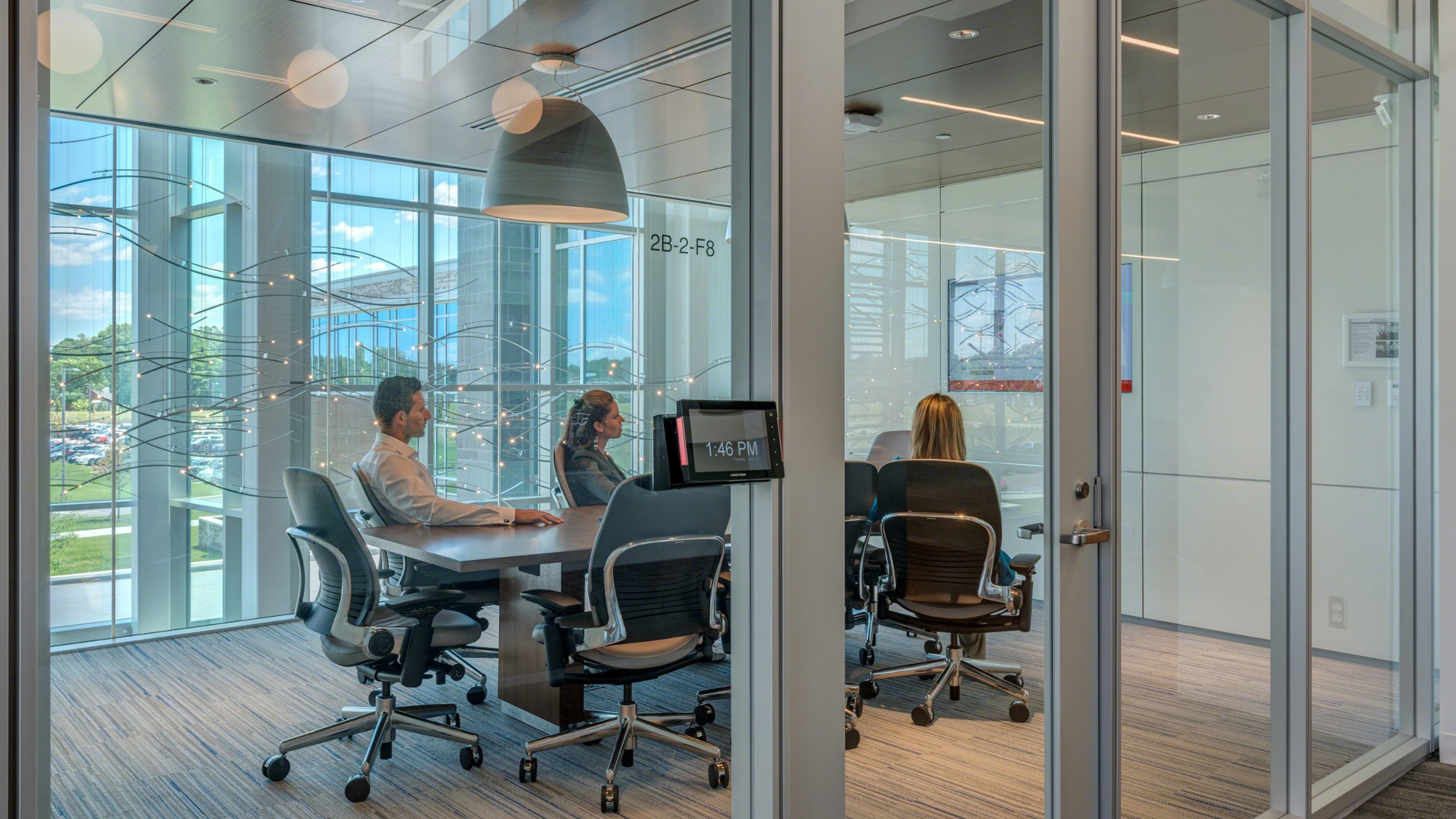 3 persons inside a meeting room with glass walls, screen on a white wall, room wizard.